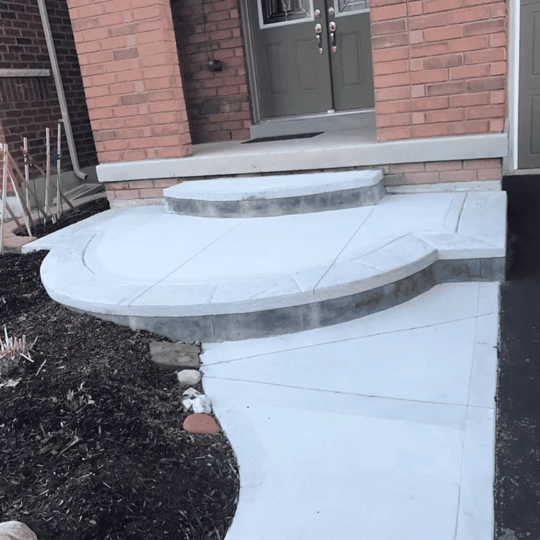Front porch and walkway made of exposed aggregate concrete with a smooth, dark-stamped border. The curved pathway blends neatly into the grass lawn, adding polished charm to the home's exterior.