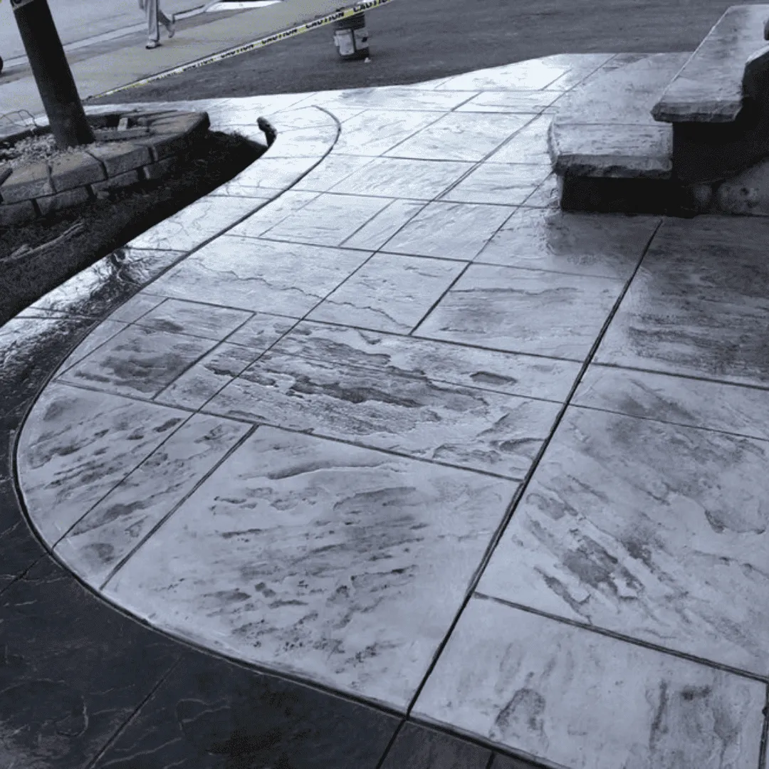 Stamped concrete walkway with a textured stone pattern and a curved edge, shown freshly sealed with a glossy finish. Designed for durability and style, enhancing the home's curb appeal.