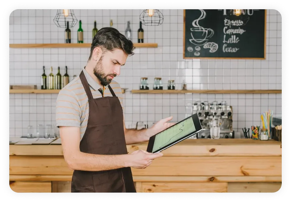 Small business owner wearing an apron and analyzing data on a tablet in a modern café, showcasing the importance of local SEO in Dallas for attracting nearby customers and driving business growth.