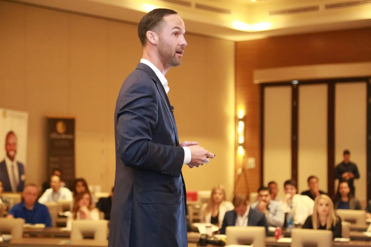 Engineering leader mid-presentation at a conference, relaxed shoulders and open posture, audience visible in soft focus
