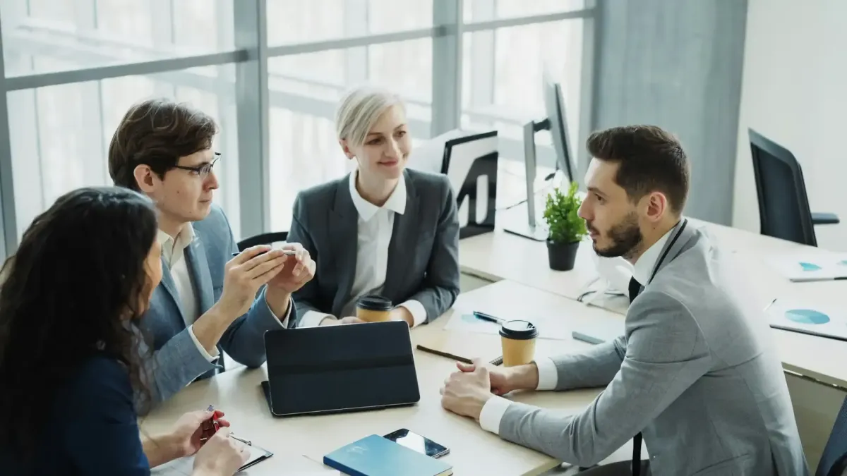 Four business professionals having an engaged discussion around a conference table in a bright modern office.