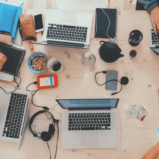 Overhead view of a cluttered work desk with multiple laptops, headphones, and personal items