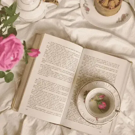 Open book with a cup of tea and a pink rose on a bed, creating a cozy reading scene