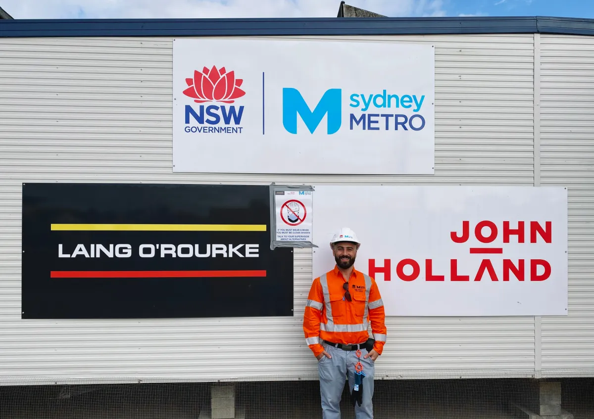 A CareerSeekers' participant standing on a project site, posing in front of partner logos during their workplace placement