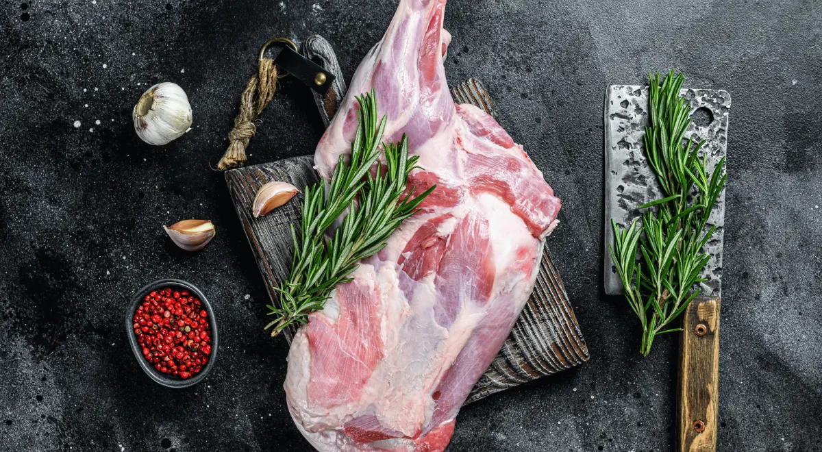Stylized cut of organic, grass-fed beef from Briarmead Farm on a wooden cutting board, garnished with fresh herbs and accompanied by a butchering knife, set against a dark background.