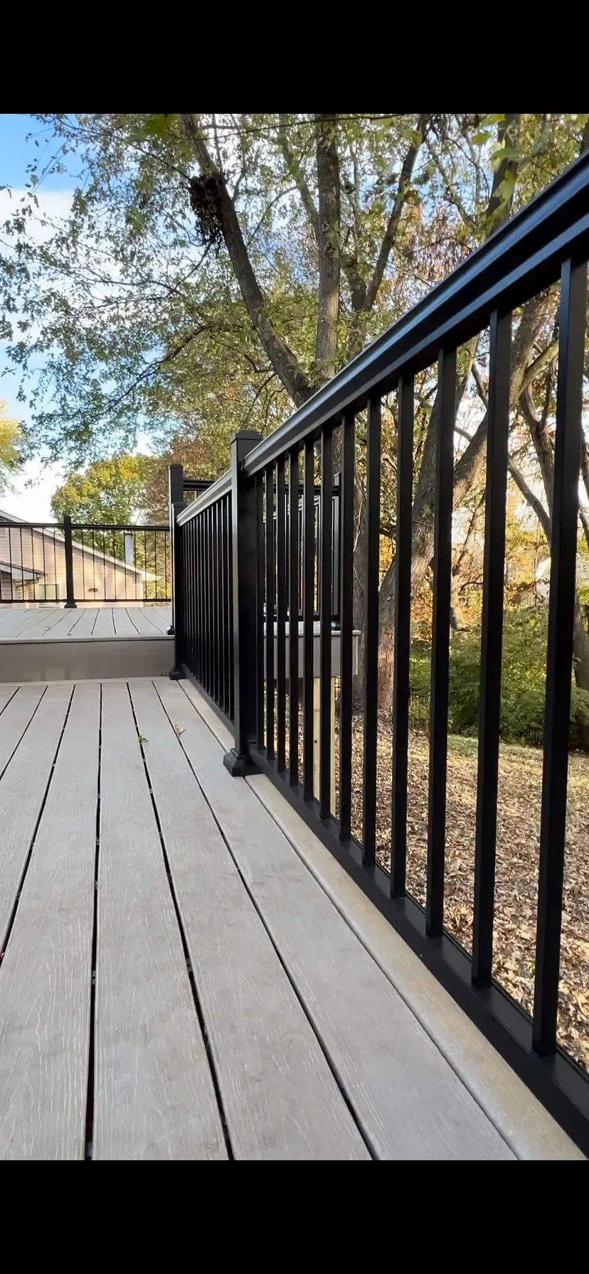 New composite deck installation in St. Louis, MO with dark aluminum railing and wooded surroundings.
