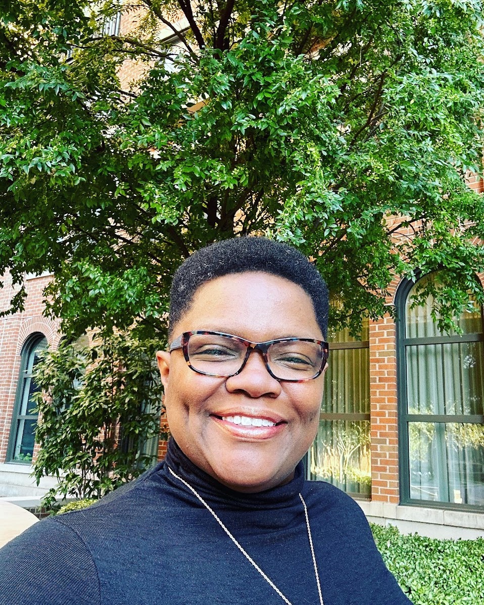 Tia A. Williams, Principal Systems-Thinking Architect and founder of The Inbound Authority System™, standing in front of a brick building. Former SVP of CFI and VP of A Cloud Guru.
