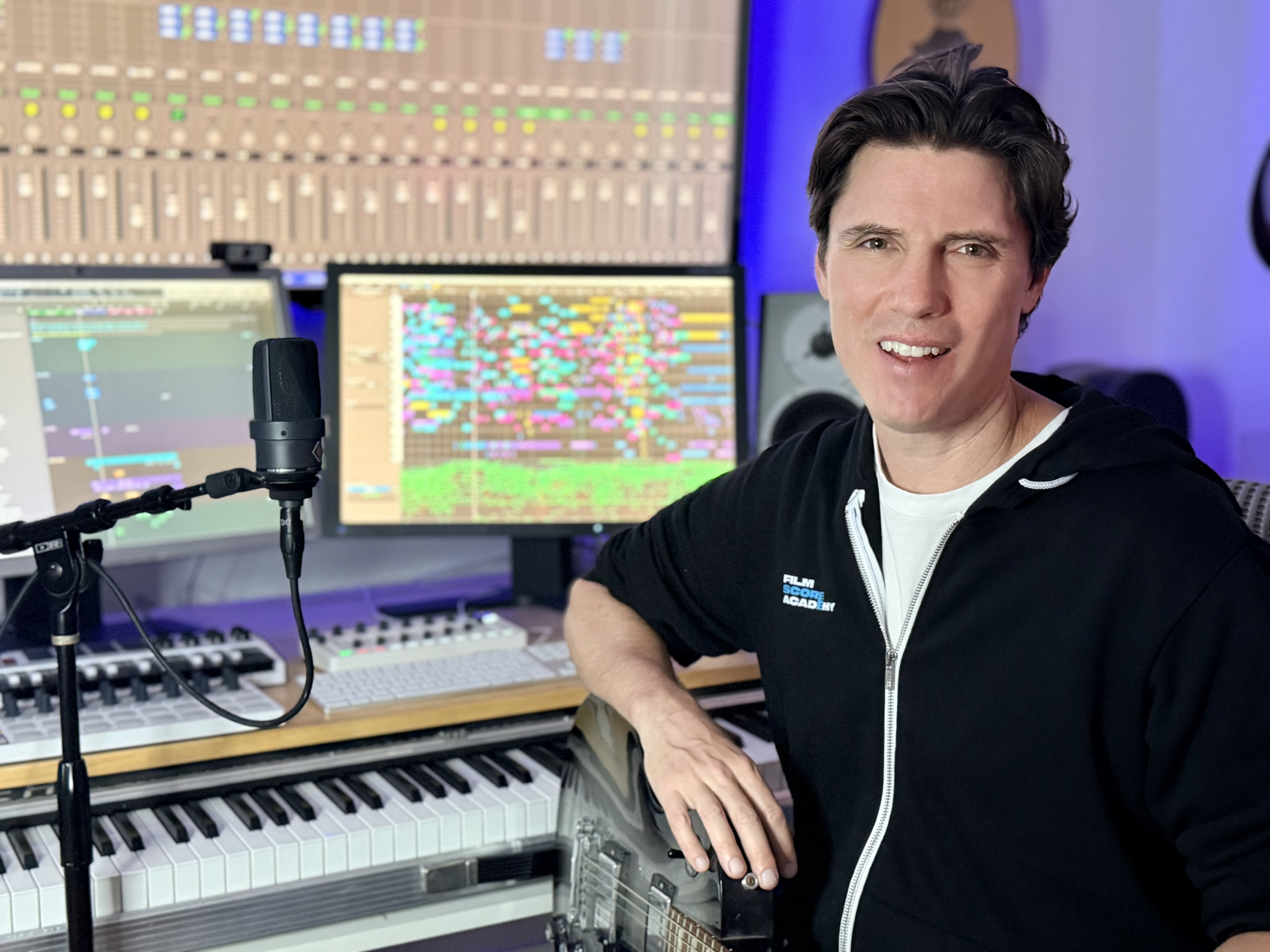 Composer Ian Honeyman in a professional film scoring studio with monitors, mixing console, MIDI keyboard, and recording equipment