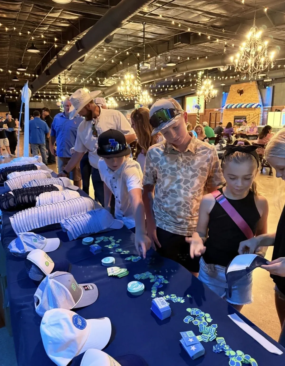 A diverse team of corporate professionals in business attire gathered around a conference table, actively discussing branded merchandise samples and event strategies. The office setting is modern, with large windows and natural light highlighting the collaborative atmosphere.