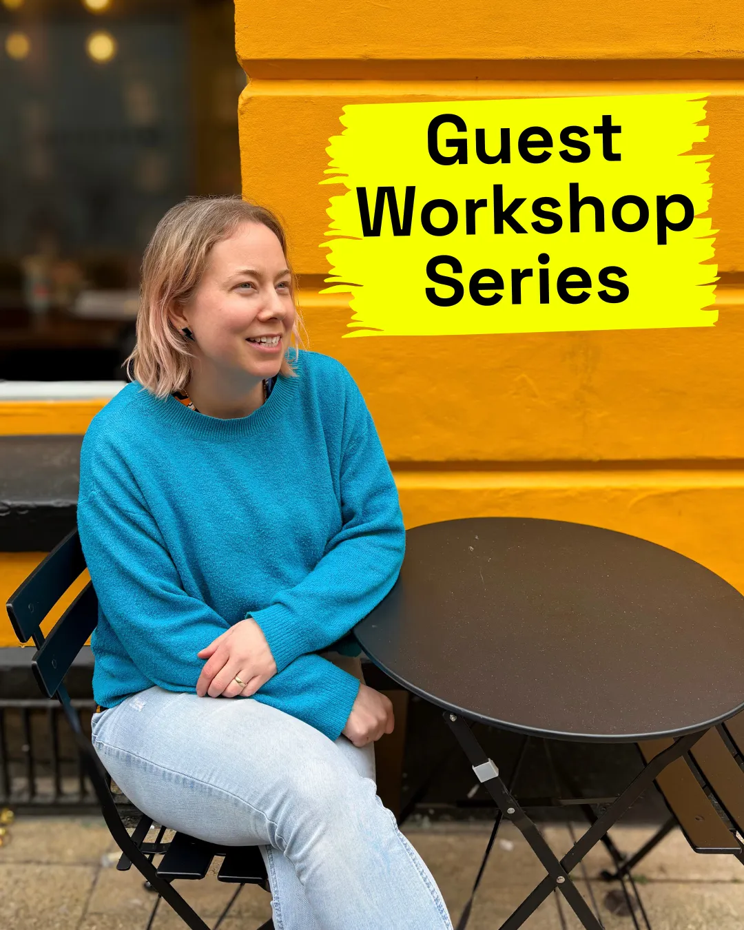 Woman wearing a bright blue jumper and jeans, sitting in front of a bright yellow wall. Black text on the wall reads Guest Workshop Series