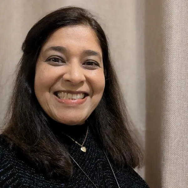 Resma smiling at the camera in front of beige curtains.
