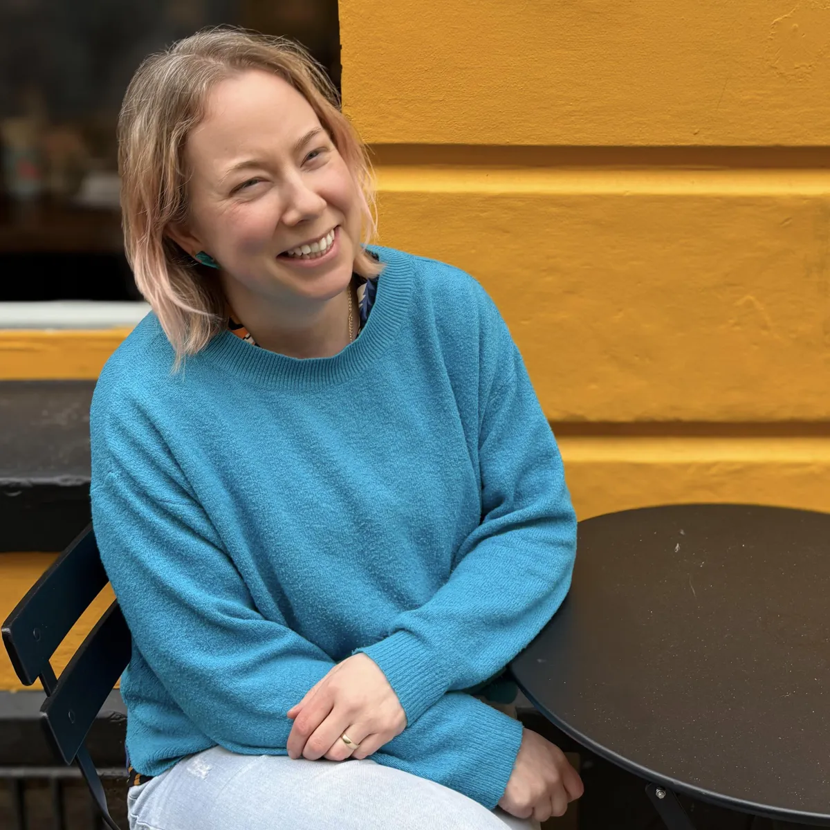 Christina Poulton sat on a chair in front of bright yellow wall.