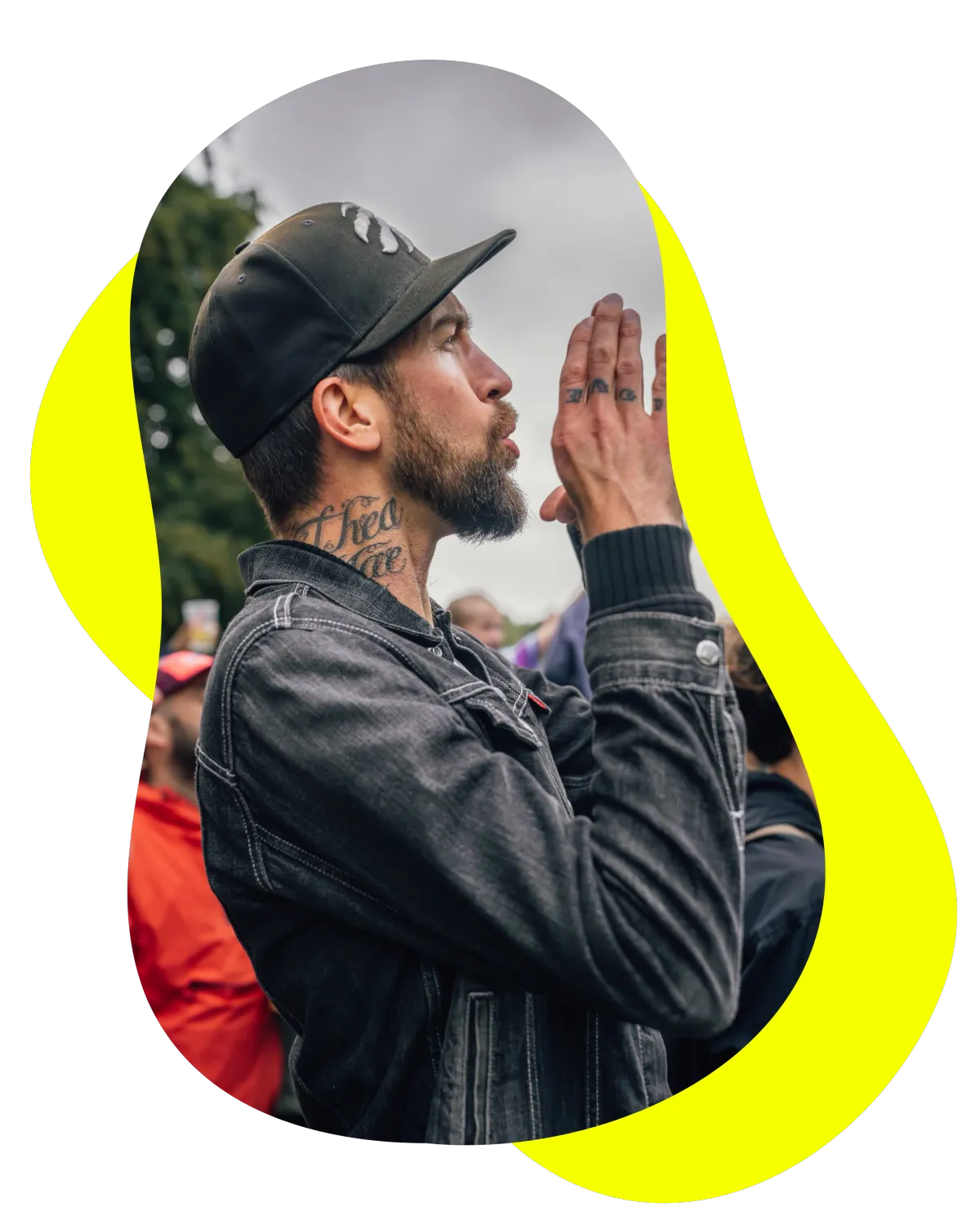 Liam Barrington-Bush from RadHR, shown in profile outdoors wearing a black cap and denim jacket, with a beard and tattoos, hands raised together mid-applause.