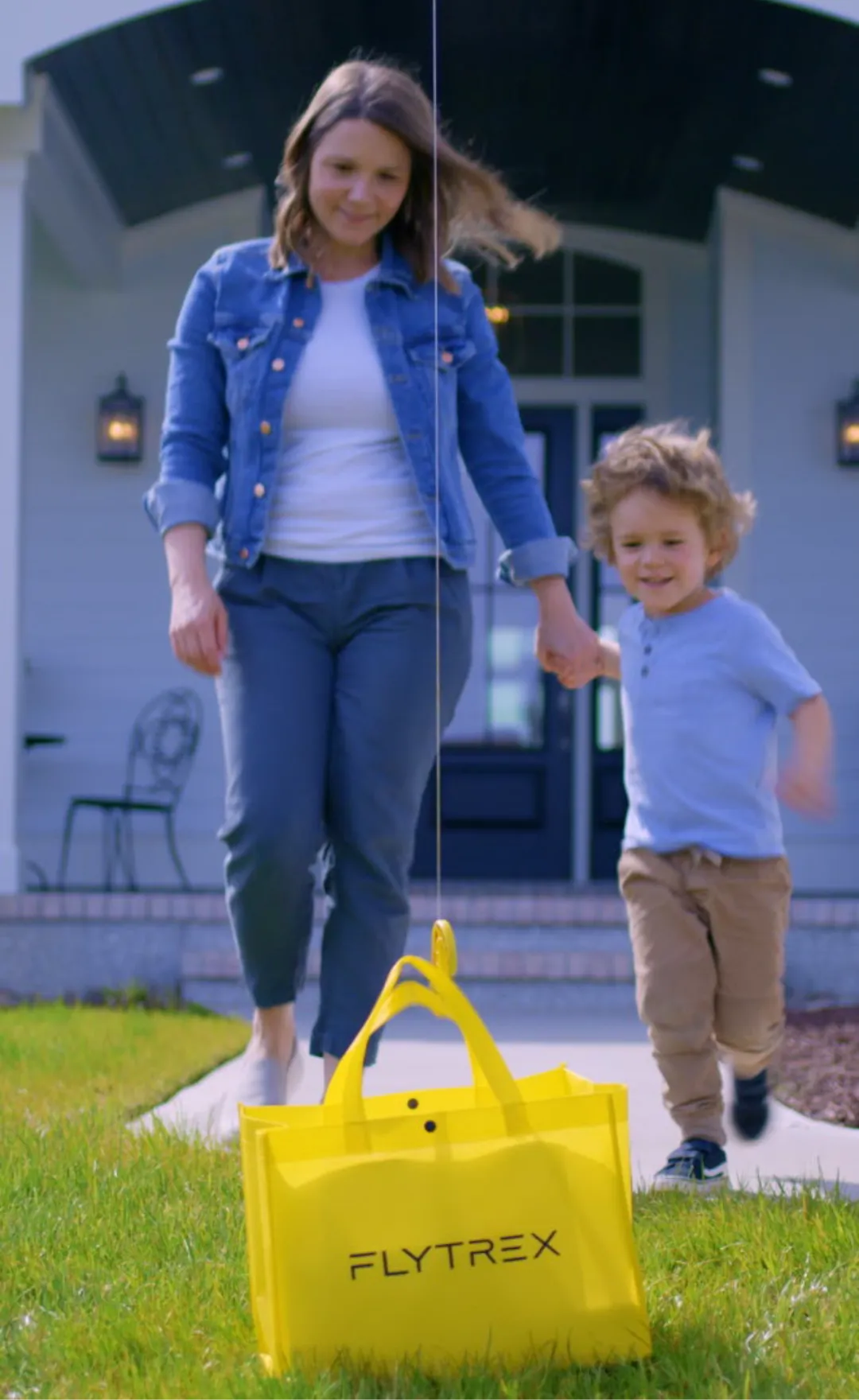 Mother and child walking toward a Flytrex drone delivery package placed on a lawn in front of a suburban home, illustrating residential drone delivery service.