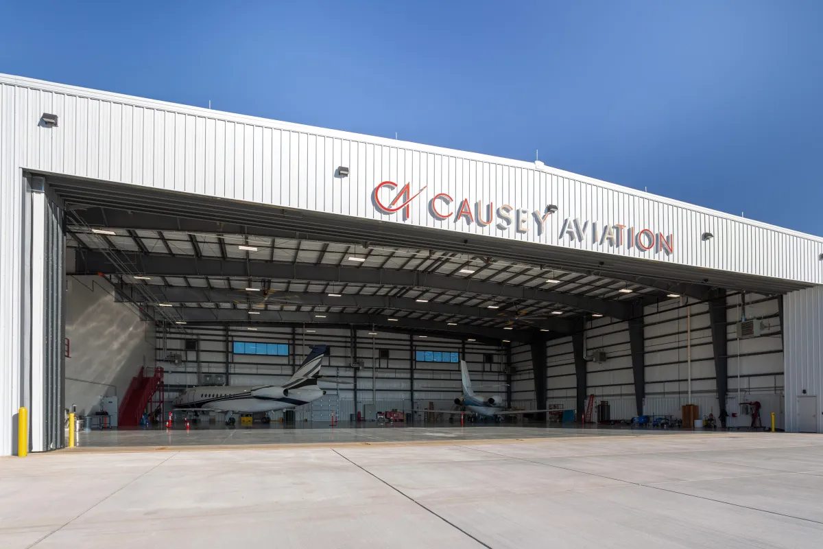 Causey Aviation aircraft hangar with open doors, private jets parked inside, and a clear blue sky at an aviation maintenance and operations facility.