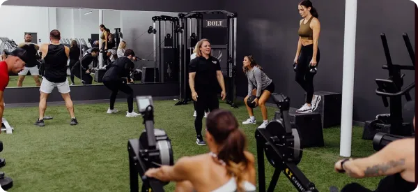 Group of people participating in a fitness class, doing squats on platforms with kettlebells under the guidance of a trainer
