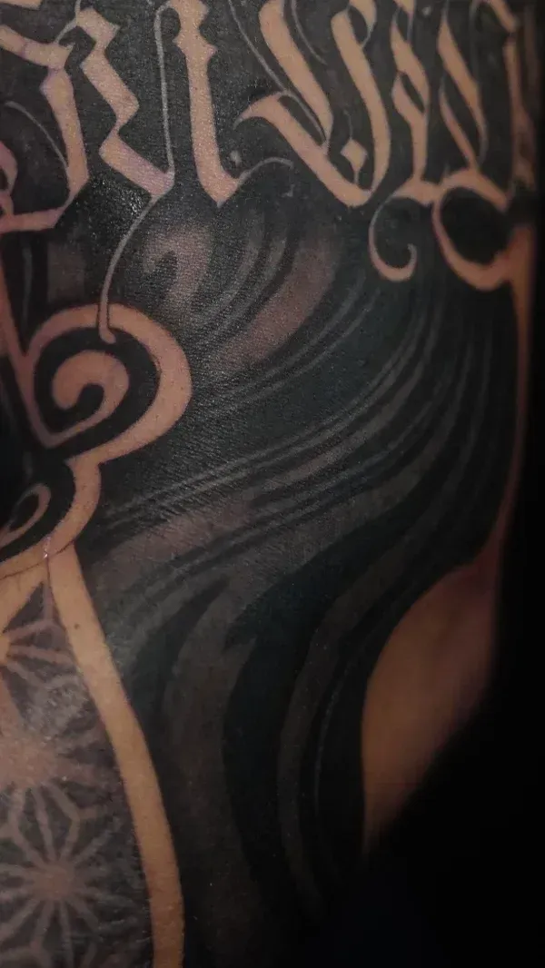 Close-up blackwork sleeve photographed in natural window light, dense saturated blacks, crisp edges, flowing composition around musculature, high-detail texture, cinematic framing emphasizing line and contrast in photorealistic style.