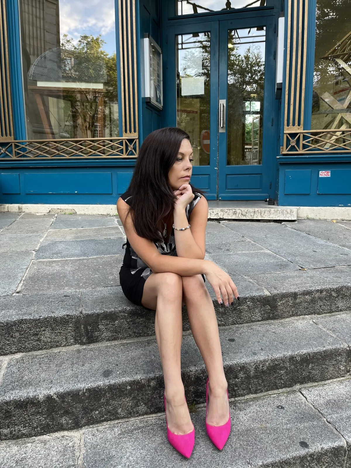 Michelle Rowlinson sitting on steps, wearing bright pink shoes, looking reflective