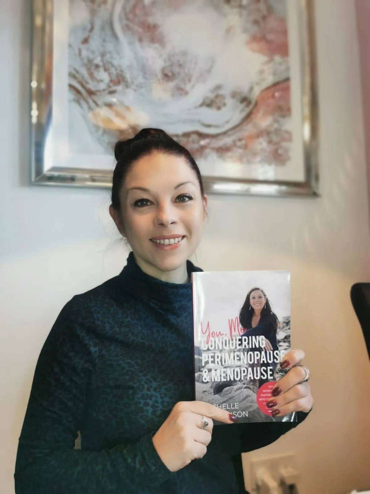 Michelle Rowlinson holding her book 'You, Me, Conquering Perimenopause & Menopause,' smiling with pride