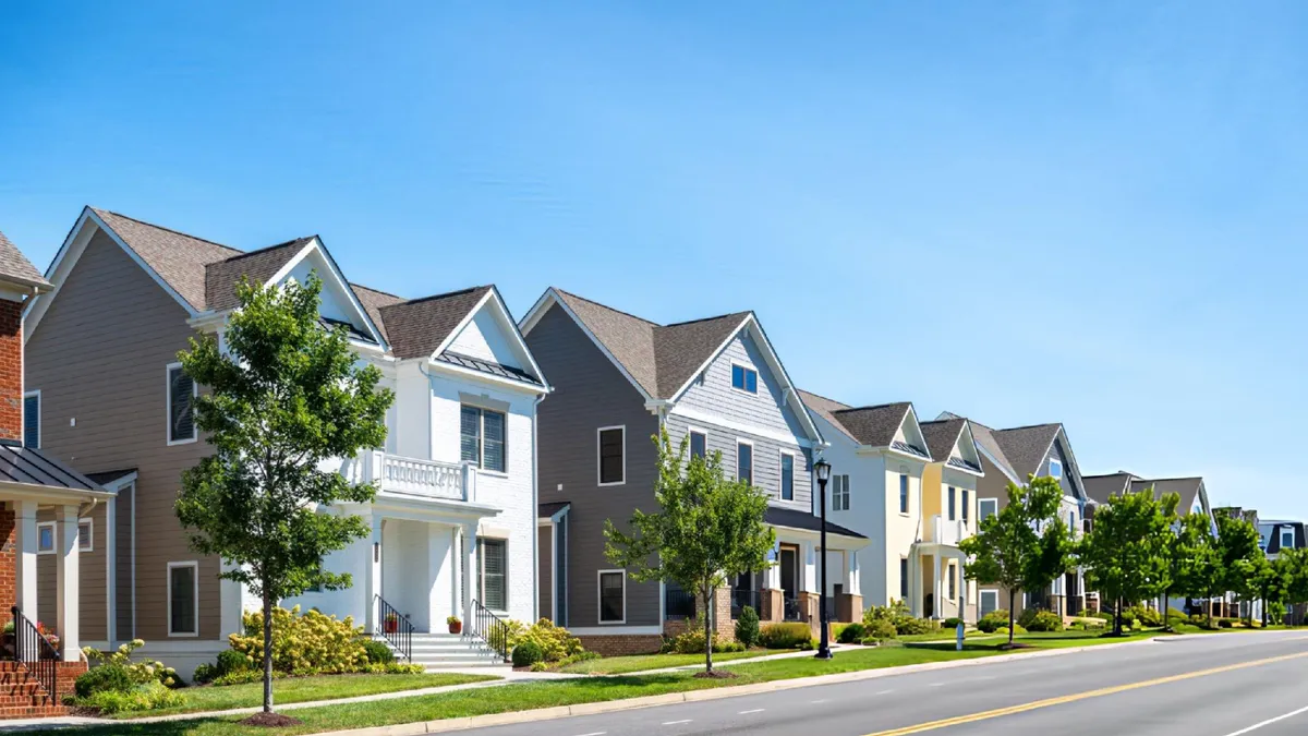 Row of suburban two-story houses with varied colors, front lawns, driveway, and clear blue sky.