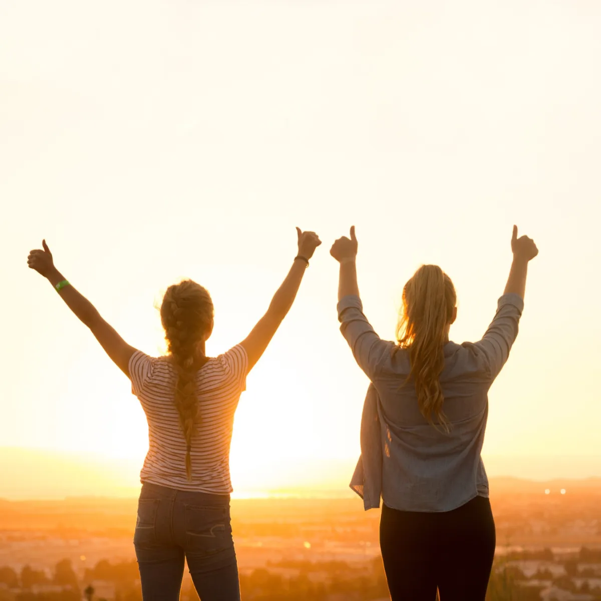 Two women giving a thumbs up looking at the sunset