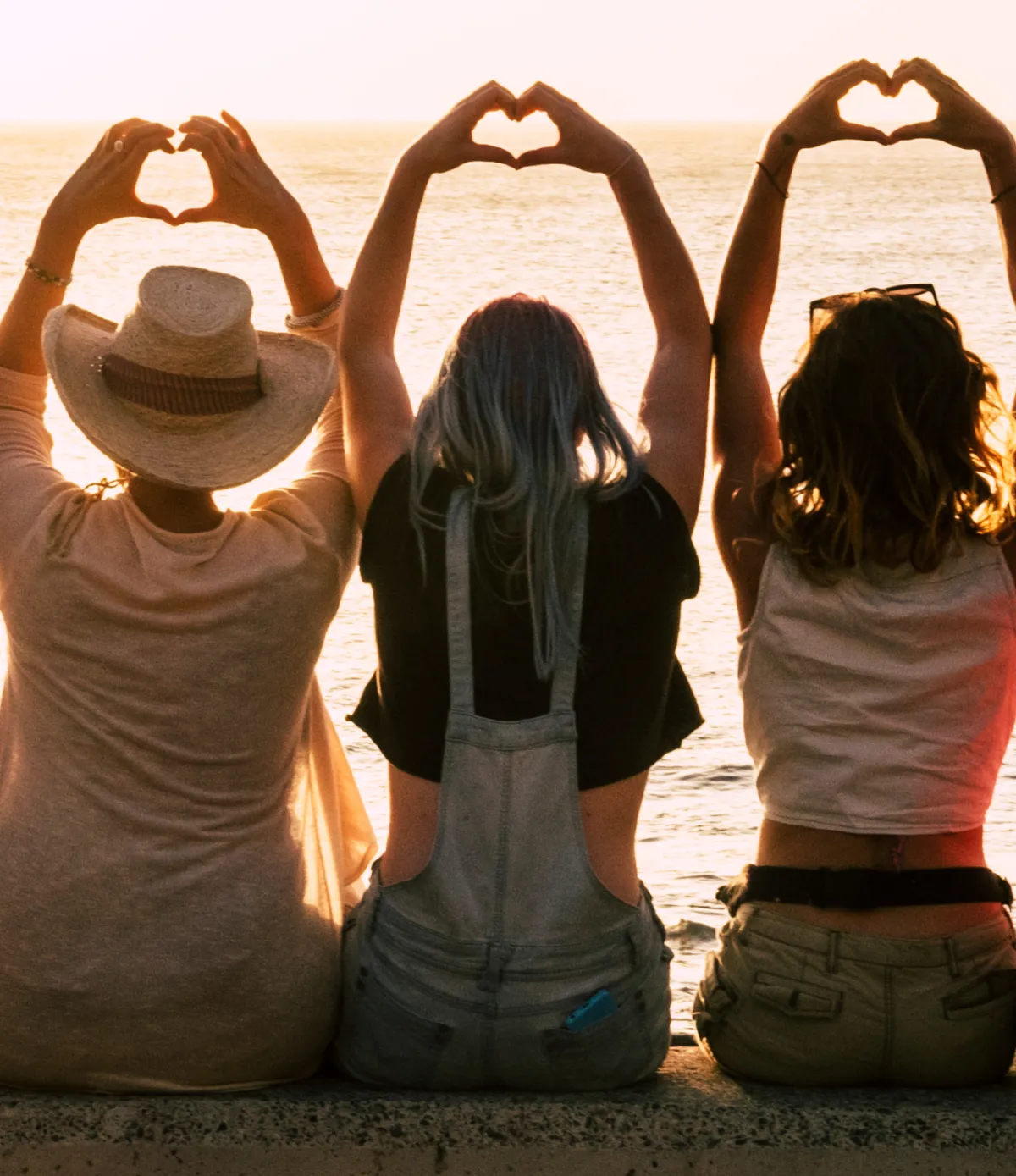 Three women, viewing the sunset making hearts with their hands in the air