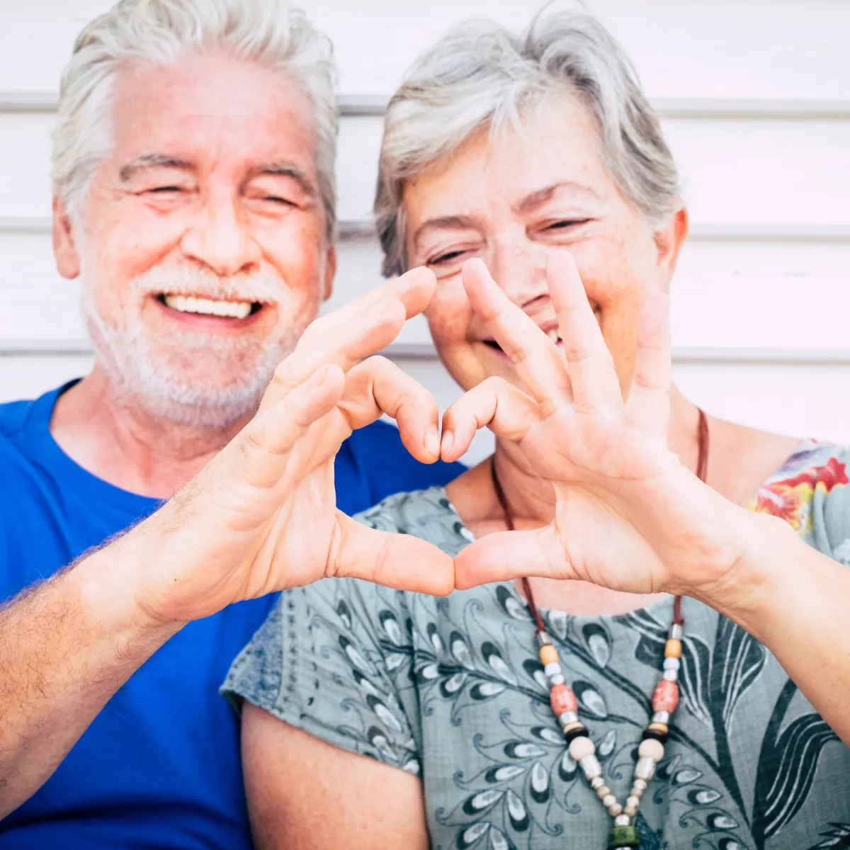 Older couple making a heart with their hands and smiling