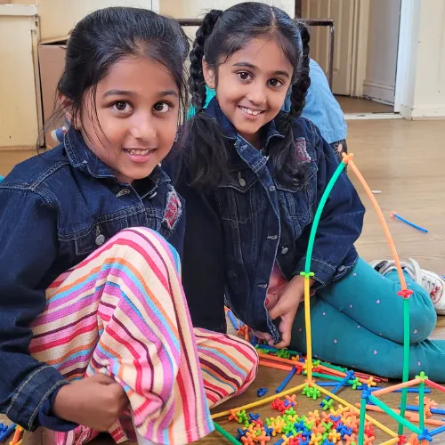Two children sitting on the floor and creating a tall structure with bright construction pieces during a TechySTEAM Explorers class.