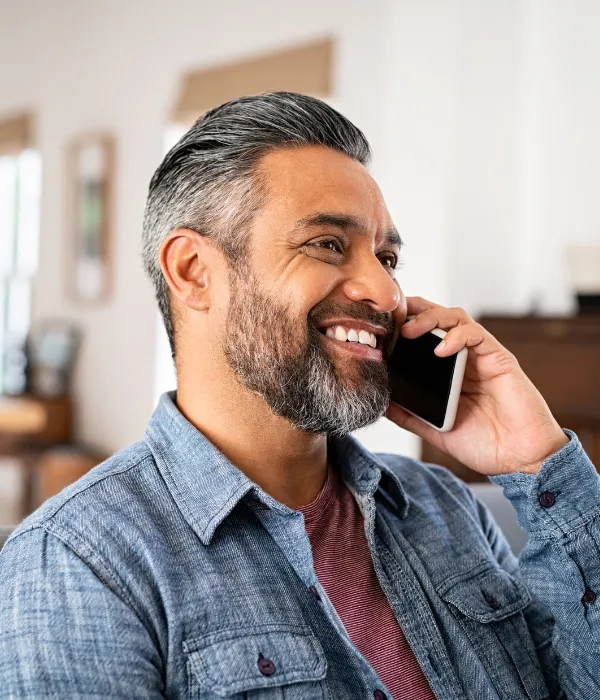 Salt and peppered man with a beard is smiling while on a mobile phone.