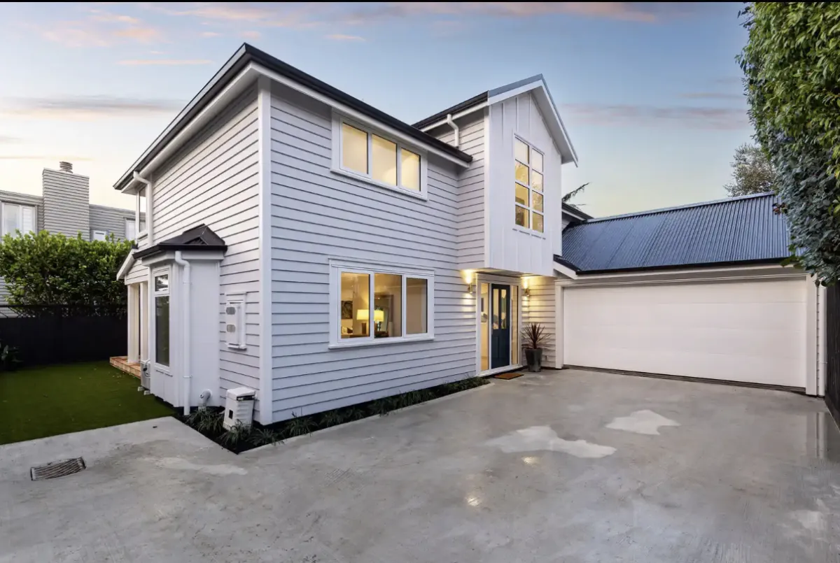 Contemporary white two-storey house with large windows and wooden fencing, set against a bright blue sky.