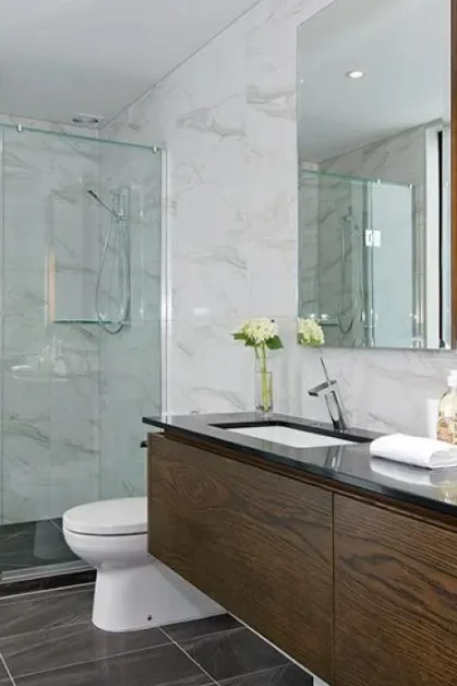 Elegant bathroom featuring a glass shower, marble-look tiles, and a dark wood vanity with dual sinks.