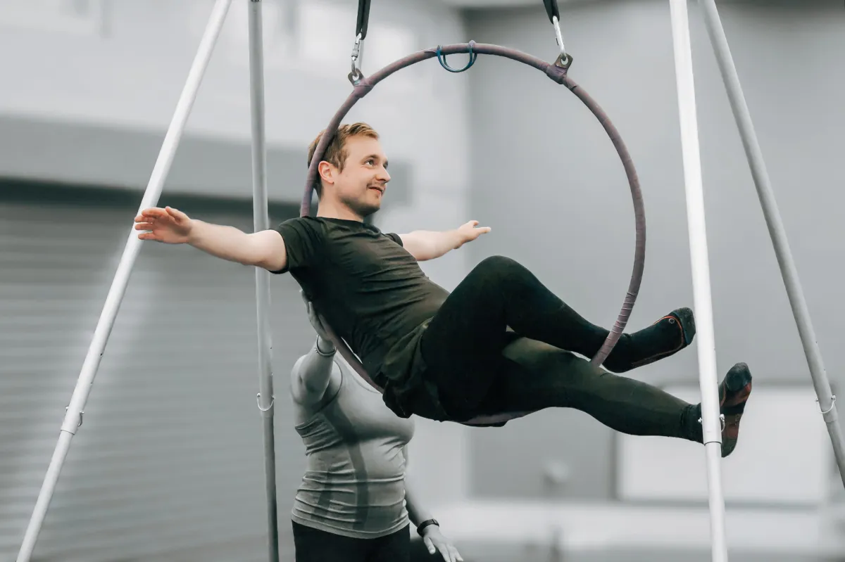 Smiling female trainer mid-lunge in a bright sunlit studio wearing lilac branded activewear, dynamic low-angle composition.