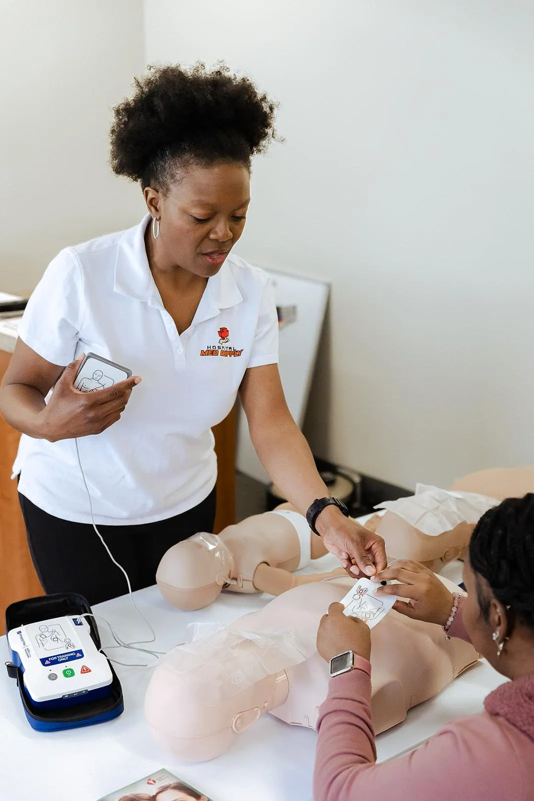 Nurse teaching student show to put AED pads on CPR manikin