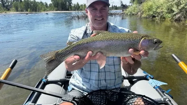 A smiling man with a beard and a baseball cap standing in a river holding a fly rod.