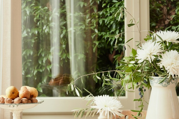 Sunlit table with fresh pears, walnuts, and white flowers by a garden window