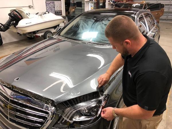 Auto film installer laying ppf film on the hood of a Mercedes
