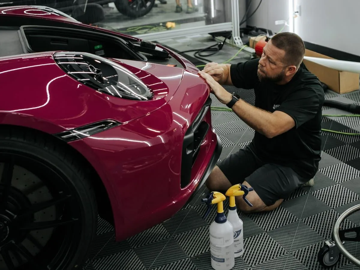 Auto film installer laying ppf film on the hood of a Porsche