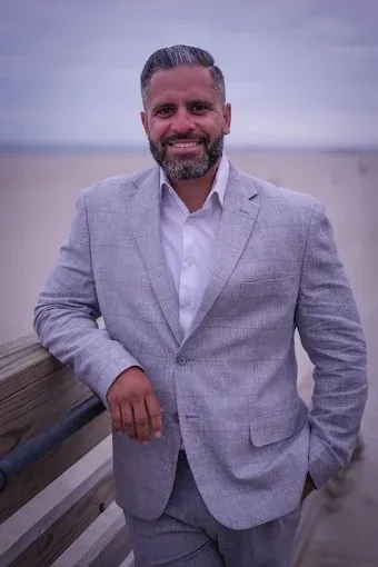 Full-body portrait of real estate agent Frank Monforte Jr. on a residential Long Island street.