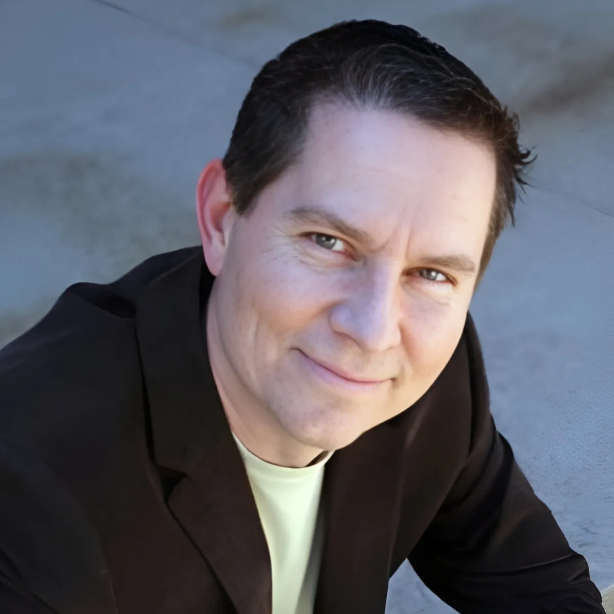 Tony Swantek in a suit, blue shirt, and red tie smiles in front of a textured brick wall.