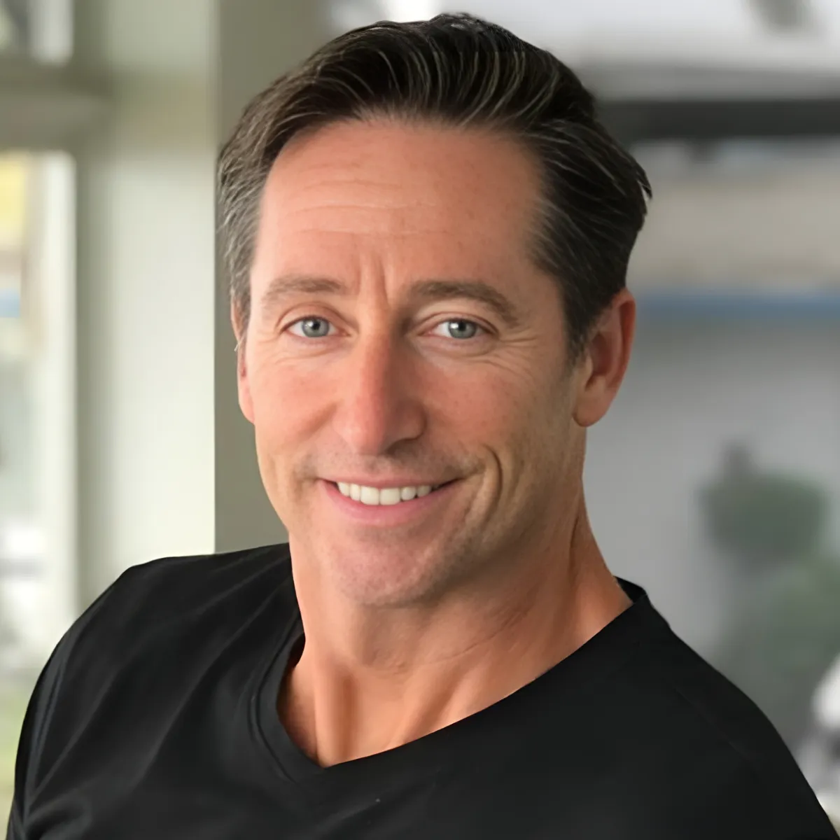 Tony Swantek in a suit, blue shirt, and red tie smiles in front of a textured brick wall.