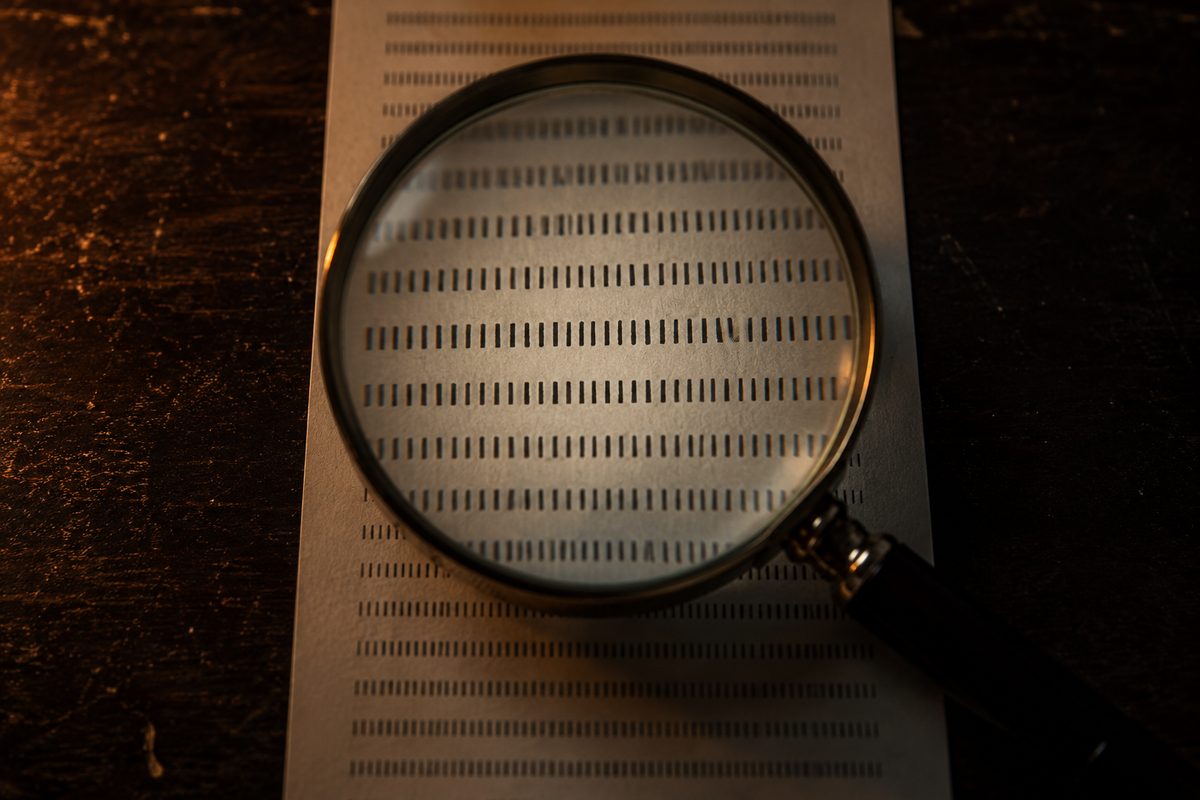 A magnifying glass resting on a printed sheet of dense text on a dark wooden desk.