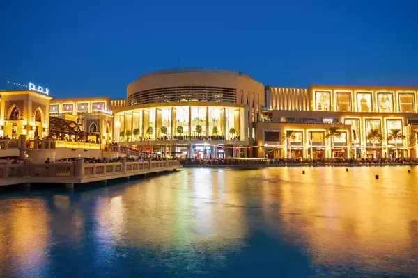 Le centre commercial Dubai Mall, illuminé de nuit, avec une vue sur l'eau, reflétant la lumière et les boutiques de luxe, dans le quartier animé de Dubai.