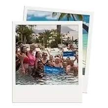 Groupe de voyageurs dans une piscine tropicale tenant une pancarte "Make Wishes Real", sourires et ambiance conviviale lors d'une Life Experience avec Travel Advantage.