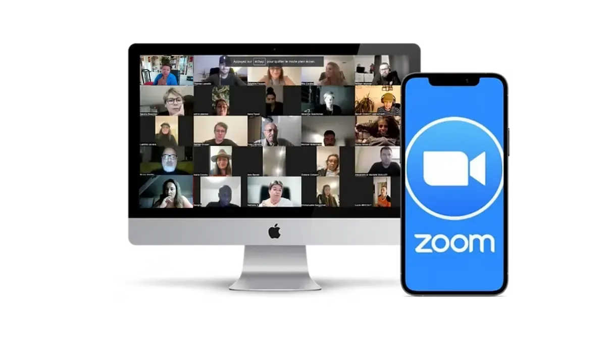 Écran d'ordinateur affichant une réunion Zoom en galerie avec de nombreux participants, à côté d’un smartphone montrant le logo bleu de l’application Zoom.
