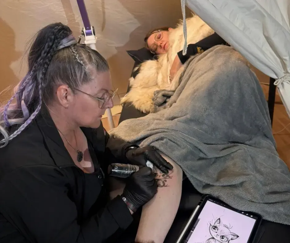 Tatouage artistique en direct au Pagan Arbor Festival à Fribourg par Magic Tattoo Ink, un chat en style sketch sur la jambe d’une cliente