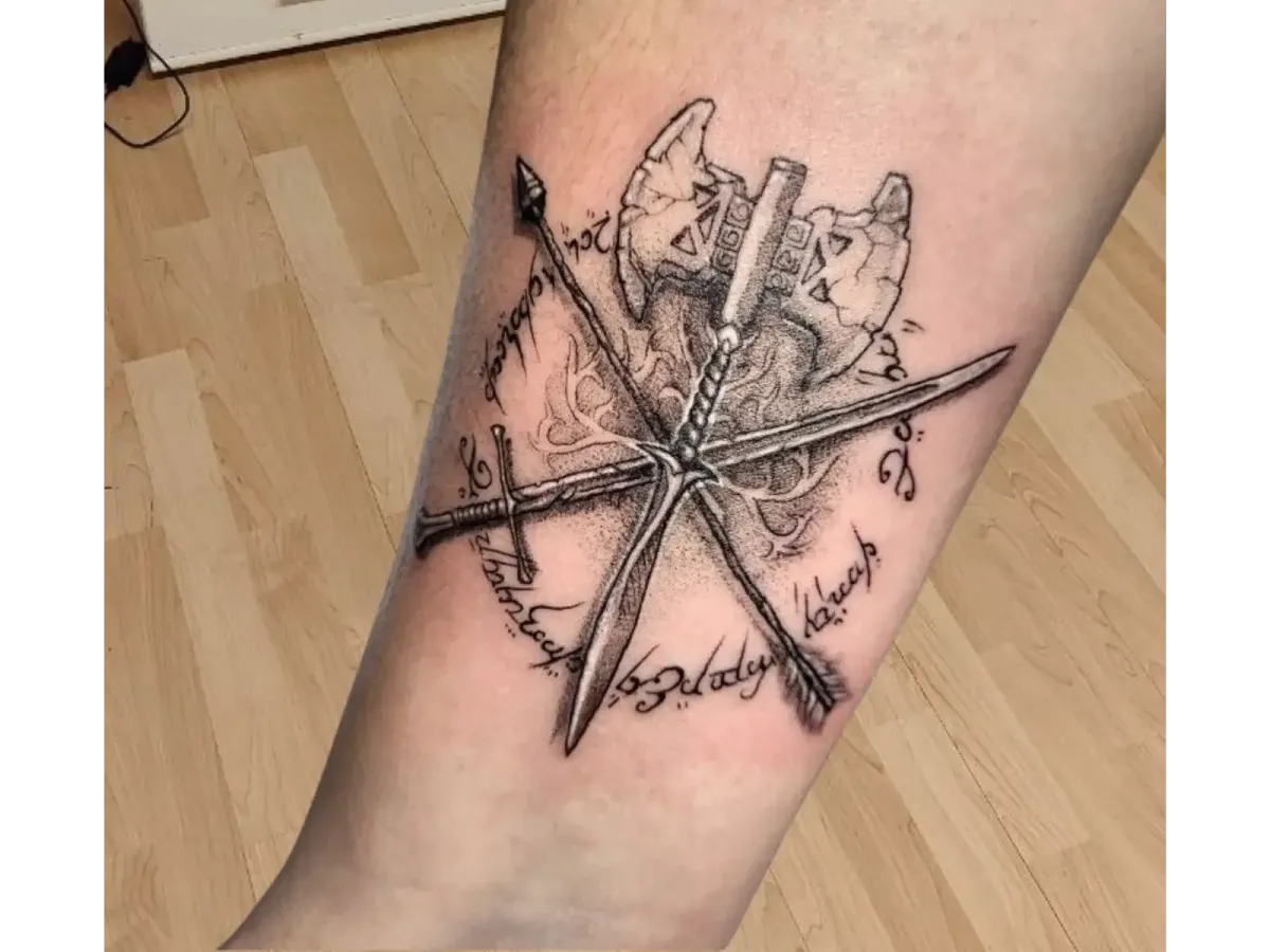 Tatouage viking noir et gris sur la jambe représentant deux haches croisées et une épée, entouré de runes et motifs nordiques – Magic Tattoo Ink