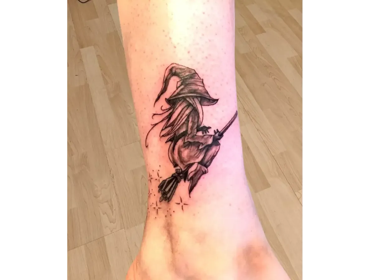 Tatouage de sorcière sur un balai en style sketch noir et gris, réalisé sur la cheville – Magic Tattoo Ink