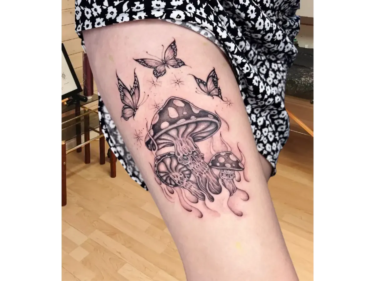 Tatouage cuisse femme avec champignons magiques, méduses et papillons en noir et gris, style onirique et détaillé – Magic Tattoo Ink