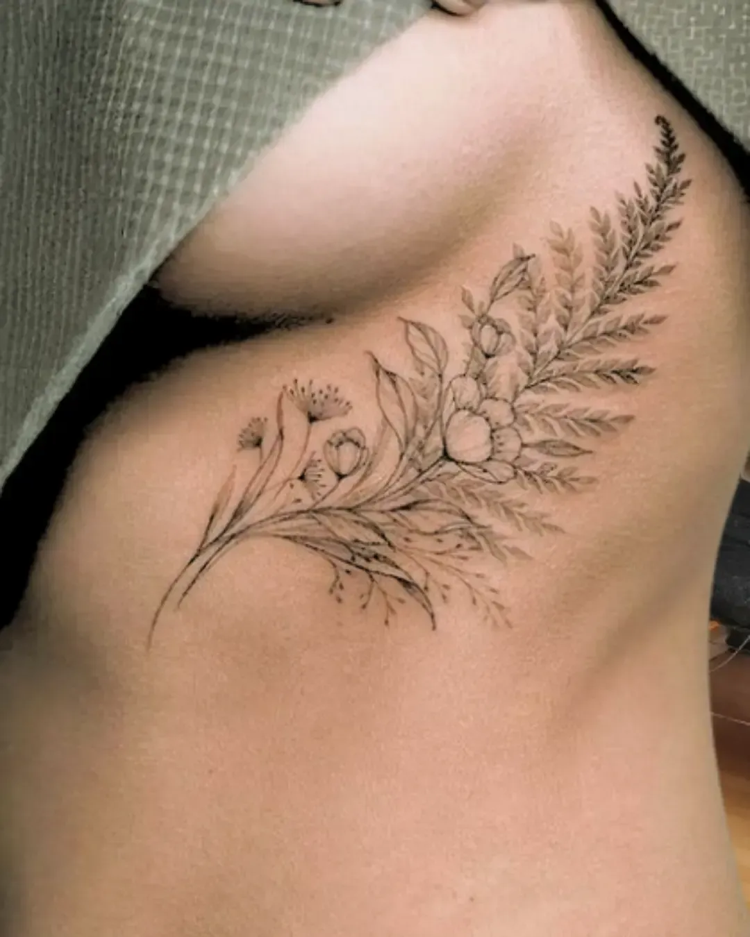 ChatGPT a dit :  Tatouage floral délicat sous la poitrine avec fougères et fleurs sauvages – design fin et féminin, symbole de nature, grâce et sensualité, réalisé par Magic Ink à Fribourg.