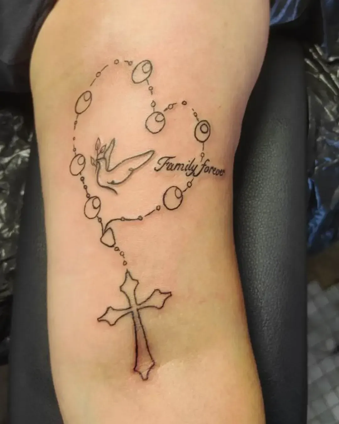 Tatouage fin d’un chapelet en forme de cœur avec colombe, croix et inscription Family forever – symbole de foi, paix et amour familial, réalisé par Magic Ink à Fribourg.